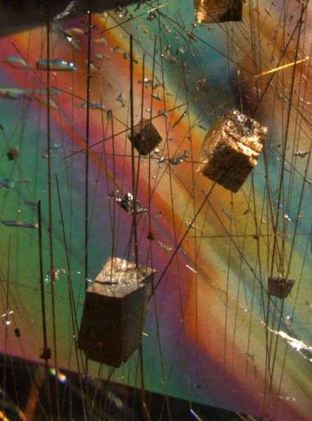 Einschlüsse von vermutlich Siderit (FeCO3) und Rutilnadeln in Bergkristall (Quarz). Fundort: Minas Gerais, Brasilien. Bei den braunen, rhomboedrischen Kristallen handelt es sich aufgrund der Morphologie und Farbe höchstwahrscheinlich um das Eisencarbonat Siderit. Die starken Interferenzfarben des ansonsten farblosen Quarzes entstehen durch die fast parallele Blickrichtung zur optischen Achse des Kristalls im polarisierten Licht. Bildhöhe: ca. 10 mm, Kombination von Auflicht (Glasfaserlicht) und Durchlicht, gekreuzte Polarisatoren, Leica MZ16 Stereomikroskop (Michael Hügi, Schweizerisches Gemmologisches Institut)