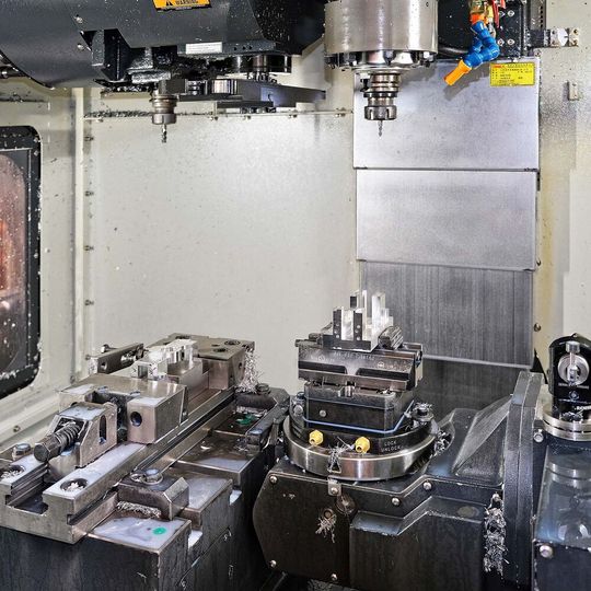 The V-30iT is unusual in that the left-hand side of the swivelling trunnion with rotary table is supported by a bearing in the side of an adjacent fixed table, so 3-axis machining and 3- to 5-axis machining on the same part can be completed without it leaving the working area. Alternatively separate jobs may be undertaken on each table. The V-30iT is unusual in that the left-hand side of the swivelling trunnion with rotary table is supported by a bearing in the side of an adjacent fixed table, so 3-axis machining and 3- to 5-axis machining on the same part can be completed without it leaving the working area. Alternatively separate jobs may be undertaken on each table.
