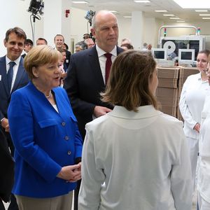 Bundeskanzlerin Angela Merkel und Ministerpräsident Dietmar Woidke im Gespräch mit Auszubildenden, begleitet von Takeda President & CEO Christophe Weber und Standortleiter Wolfgang Eck. 