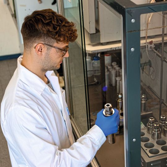 Frank Sailer bestückt den Heizblock mit einem Reaktionsgefäß für die Ein-Topf-Synthese. (Bild:  Dr. Robert Pazdzior)