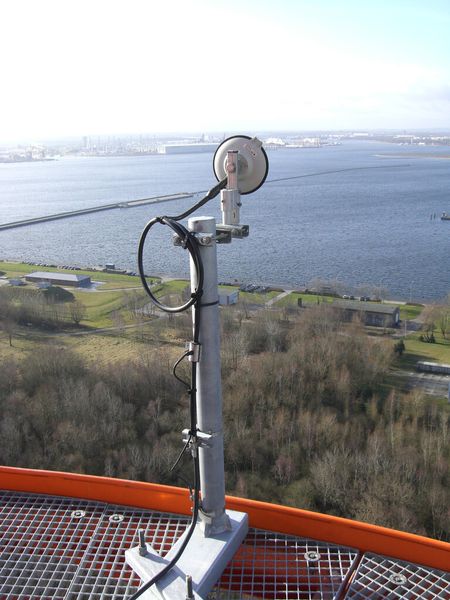 Blick von Pseudolite 6 in das Testgebiet von SEA GATE am Fährhafen Rostock. In der oberen Bildmitte ist die kleine tellerförmige Antenne zu sehen, über die das Galileo-Signal abgestrahlt wird. Im Bildhintergrund rechts befindet sich der Fährschiff-Anleger. (Bild: EADS RST)