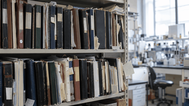 Abb. 1: Überfülltes Regal mit Papierlogbüchern und Ordnern im Laboralltag – Symbolbild für analoges Wissensmanagement.(Bild:  KI-generiert)