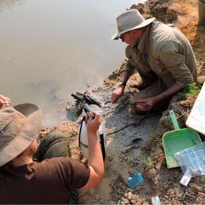 Professor Larry Barham (pictured, right) uncovering the wooden structure on the banks of the river with a fine spray(Source:  Professor Geoff Duller, Aberystwyth University)