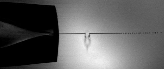 Abb. 2 Ein Infrarot-Laser trifft einen Mikroflüssigkeitsstrahl (Durchmesser etwa 10 µm; Länge des kontinuierlichen Bereichs bis der Strahl in Tröpfchen zerfällt ist etwa 1,5 bis 2 Millimeter) und setzt geladene Biomoleküle direkt aus der flüssigen wässrigen Phase frei für eine Massenanalyse.  Bild: Aufnahme mit einer Hochgeschwindigkeitskamera in Kooperation mit Dr. B. Stasicki, DLR Göttingen (Archiv: Vogel Business Media)