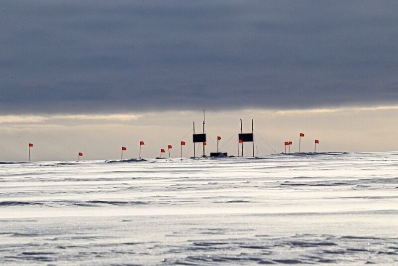 Die erste Station des Radio-Neutrino-Observatoriums auf dem grönländischen Eis. Die roten Fahnen markieren unterirdische Antennen, die von Solarmodulen (dunkle Rechtecke) mit Strom versorgt werden.  (RNO-G, Cosmin Deaconu)