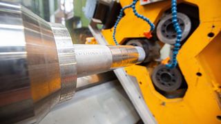 Drückwalzen: Die Spindel (vorne links) dreht das Stahlbauteil, das von den drei Walzen im Hintergrund umgeformt wird. Die blauen Leitungen sorgen für ausreichend Kühlschmierstoff. (Fraunhofer IEM)