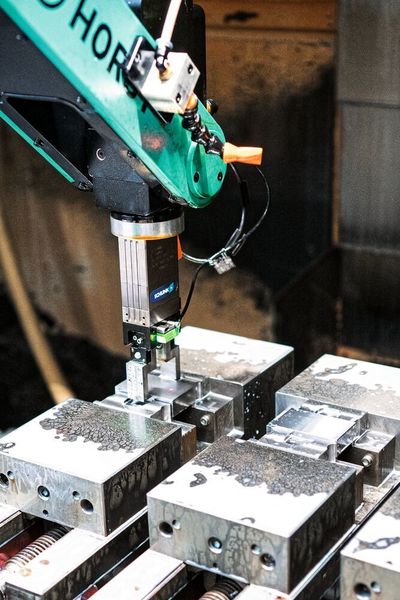 Horst fährt an den ersten von vier Schraubstöcken und öffnet diesen über ein Pneumatikventil, entnimmt das Teil und verfährt mit ihm zu einer Vorrichtung mit Luftdüsen in der Maschine, wo es direkt getrocknet wird. Anschliessend befüllt der Roboter den Schraubstock mit einem neuen Rohteil. (Fruitcore Robotics)