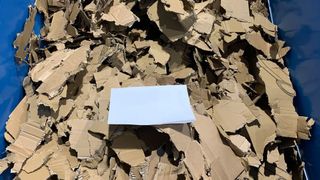 Nachdem der Kartonzerkleinerer EKZ die Kartonagen in etwa DIN A4-große Stücke zerkleinert hat (das weiße Blatt soll die Dimensionen veranschaulichen), werden sie automatisch zur Ballenpresse transportiert. (Bild: Erdwich)