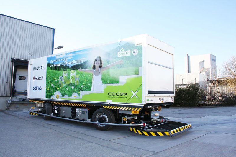 Während das Fahrzeug sich an die unterschiedlich hohen Rampen der einzelnen Hallen andockt und mittels eines Kettenförderantriebs vollautomatisch 14 Paletten einzieht, fährt ein Ladefinger aus und versorgt den Akku während der Beladung mit Ladestrom.  (Bild: Kamag)