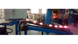 Ein Mitarbeiter entnimmt die geschmiedeten Stahlkugeln von einer Abfuhrrutsche, die im Werkzeugraum integriert ist. (Schuler)