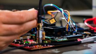 Platzierung des Chips auf der Testplatine: Tim Fritzmann hält den Chip mit einer Pinzette, um diesen anschließend auf der Testplatine zu platzieren. Über den Prozessorsockel kann der Chip schnell aus- und eingebaut werden. (Bild: Astrid Eckert / TUM)