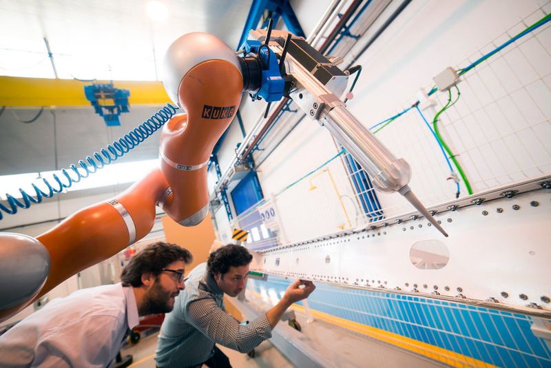 José Navarro, IDPSA, und José Saenz vom Fraunhofer IFF prüfen, wie VALERI das Dichtmittel auf ein Flugzeugbauteil aufgebracht hat. (Bild: Kuka)