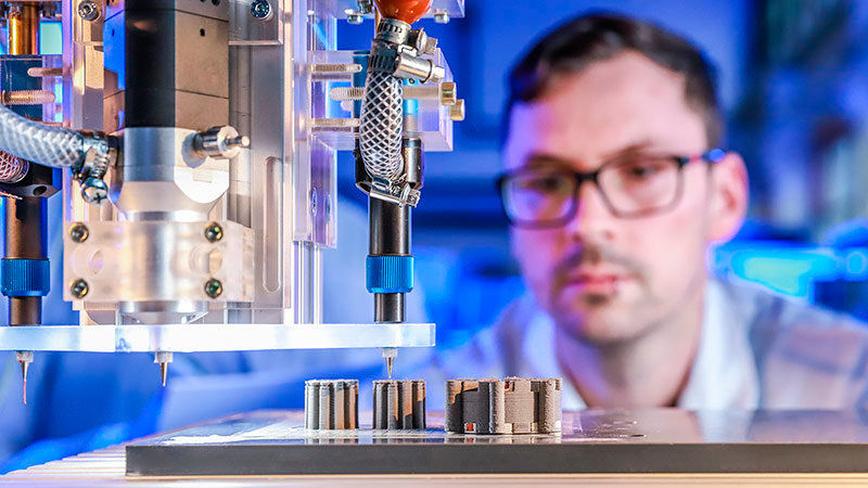Im Labor: Johannes Rudolph überwacht den 3D-Multimaterialdruck eines E-Motors, bei dem erstmals Kupfer, Keramik und Eisen gleichzeitig in einem Druckprozess zum Einsatz kommen. Links sind die Rotoren zu erkennen, rechts der Stator.   (Bild: Jacob Müller)