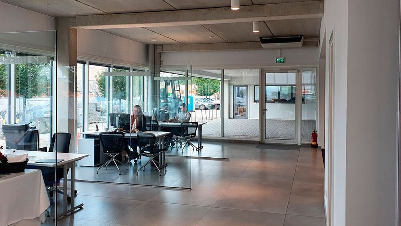 Die Gebrauchtwagenverkäufer sitzen anders als früher jetzt auch im Showroom. Gleich hinter ihnen ist eine überdachte Ausstellungsfläche zu sehen, in der ausgewählte Gebrauchtwagen besonders in Szene gesetzt werden sollen und ein separates Büro, in dem ein Fahrzeugbewerter sitzen wird.  (Bild: Mauritz/»kfz-betrieb«)