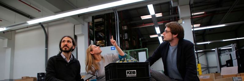 Die Navigation des Transportsystems erfolgt über die Deckenbeleuchtung. Dr. Alexandre Bousaid, Bianca Miene (beide Osram) und Tommy Falkowski (Fraunhofer IEM) diskutieren die Technologie. (Bild:  Fraunhofer IEM)