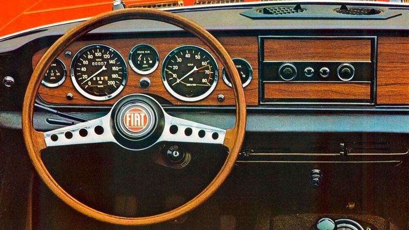 Klassische schöne Stilikone: das Cockpit des Fiat 124 Sport Spider im Modelljahr 1967. Trotz der geringen Abmessungen von 4030 mm × 1625 mm × 1420 mm lobten zeitgenössische Tester das Platzangebot im Innenraum, wobei es jedoch zu beengter Beinfreiheit im Fond kam, wenn die Vordersitze weit zurückgeschoben waren.  (Bild: Fiat)