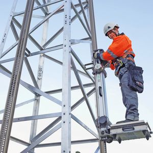 Das Bild zeigt den tragbaren High-Step-Lift im Einsatz an einem Hochspannungsmast, befestigt mit zwei High-Step-Schienen.