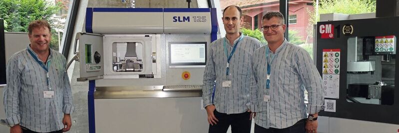 Michel Godel, Frank Gersbach et Frédéric Freiburghaus devant la machine SLM 125 de fabrication additive métallique exposée dans le showroom d'Urma. 