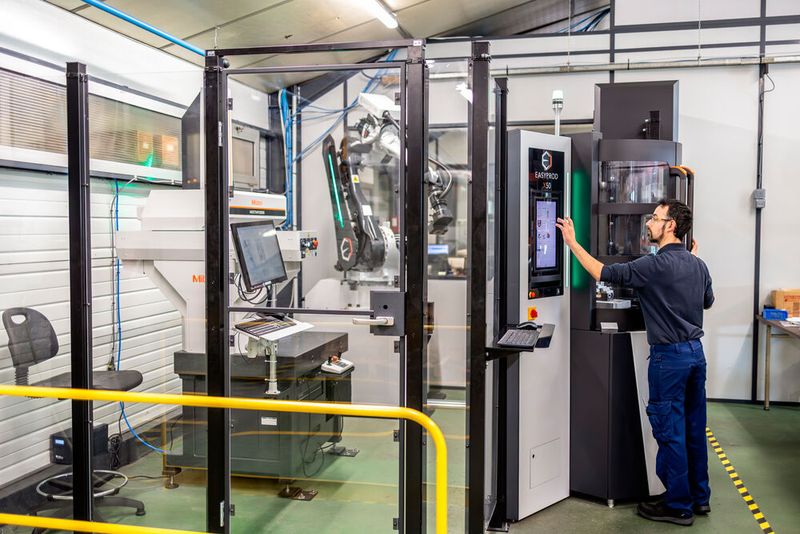 Der Roboter in der Messzelle lädt die zu prüfenden Teile in den Lagerbereich. Dann entnimmt er nacheinander die gelagerten Paletten und platziert sie auf dem Arbeitstisch der Koordinatenmessmaschine. Eine Spannvorrichtung (hier zu sehen) gewährleistet die präzise Positionierung und die ausreichende Stabilität während des gesamten Messvorgangs. (Bild: Mitutoyo)