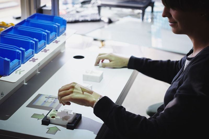 Der Arbeiter wird durch einen Beamer angeleitet, die richtigen Arbeitsschritte vorzunehmen. Zusätzlich überwachen Sensoren und eine 3D-Kamera die Aktivitäten beim Greifen der Einzelteile und beim Montieren der Baugruppe. Der Workflow und alle Funktionen werden identisch wie beim Robotermodul per App geladen und gestartet. (Bild: Ulixes Robotersysteme)