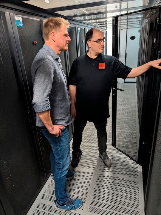 Holger Grauer, Geschäftsführer der Aixit GmbH, zeigt Gunnar Schomaker, wie DLC-Racks (Direct Liquid Cooling) Abwärme bereitstellen können.  (Bild:  SI-Lab – Uni Paderborn)