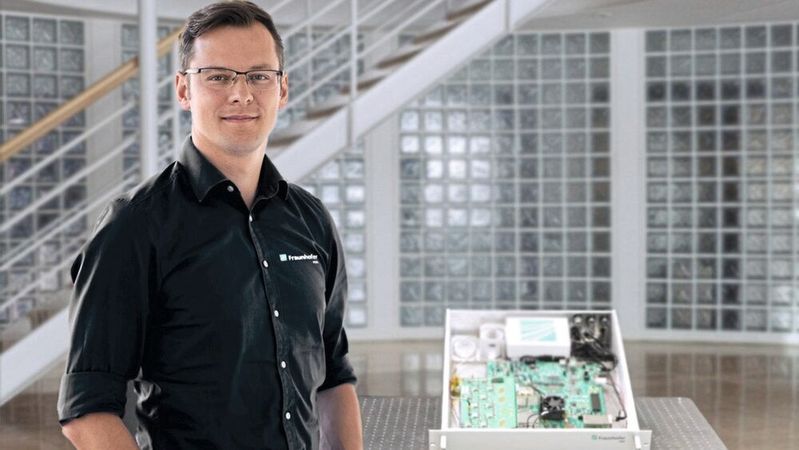 Dr. Alexander Noack steht neben dem QRNG-R19-Demonstrator. Dieser Quanten-Zufallszahlengenerator gewinnt echte Zufälligkeit aus Quanten-Vakuumfluktuationen. Auf Basis von intrinsisch zufälligen und unbeeinflussbaren Quanteneffekten werden echte Zufallszahlen mit Bitraten von 4 GBit/s erzeugt.(Bild:  Fraunhofer IPMS)