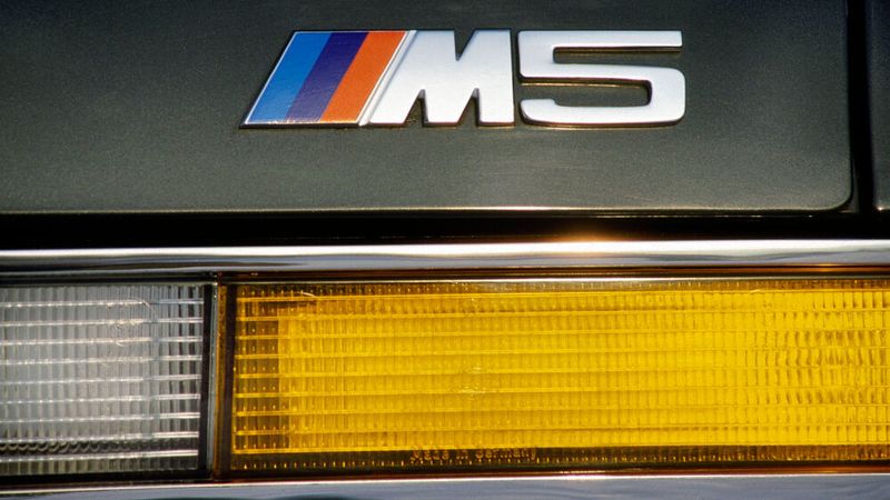 Morgens Rennstrecke, mittags Business-Lunch, dafür stand der 1985 eingeführte M5 laut BMW-Werbung. Die Magie des „M“ bemerkten auch die BMW-Händler, bei denen das in den Rennfarben blau, violett und rot gestaltete Emblem der BMW Motorsport GmbH zu den populärsten Ersatzteilen zählte: Das nur 20 Mark teure Teil zierte auch viele harmlose Basistypen wie den 518i oder 316 (E30). (Bild: BMW)