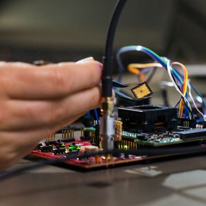 Platzierung des Chips auf der Testplatine: Tim Fritzmann hält den Chip mit einer Pinzette, um diesen anschließend auf der Testplatine zu platzieren. Über den Prozessorsockel kann der Chip schnell aus- und eingebaut werden.(Bild:  Astrid Eckert / TUM)