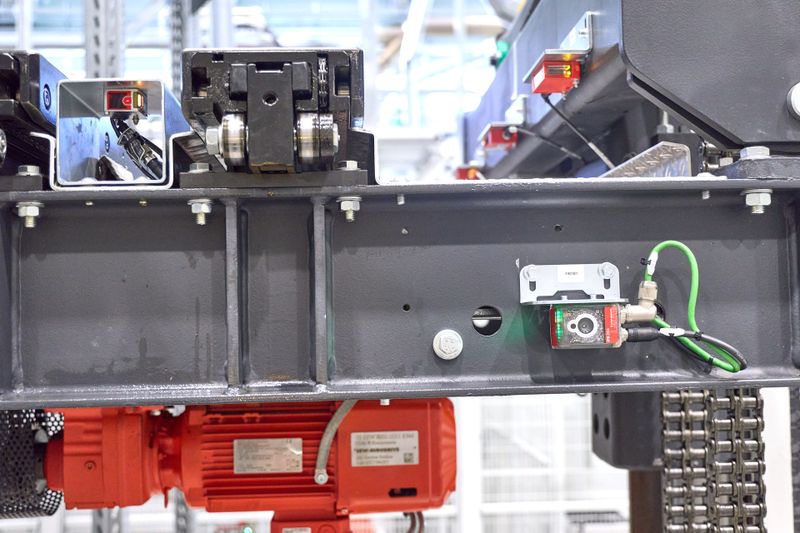 Leuze Sensorik unterstützt auch bei der Fachfeinpositionierung: Ein am RBG befestigter kamerabasierter Sensor IPS 200i fokussiert dazu auf einen am Regal angebrachten Reflektor, er eignet sich für Positionieraufgaben von 100 bis 600 Millimeter Abstand. Reflexionslichtschranken (oben rechts) erfassen zudem die Anwesenheit der Gestelle auf dem RBG. (Bild: Leuze)