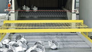 Aluminiumdruckgussteile am Auslauf einer Drahtgurt-Strahlanlage. Mit diesem Anlagentyp lassen sich Massenteile kontinuierlich mit Aluminium strahlen. (Agtos)