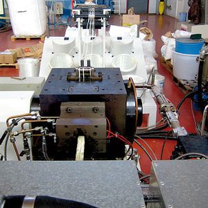 Bild 1: Scheiben-Schmelzepumpe, bei der oben drei weiße Faserstränge eingezogen werden. Der Ausstoß der mit Thermoplast benetzten Endlosfasern erfolgt seitlich.