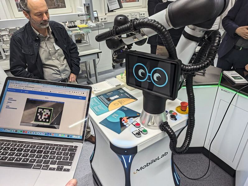 Das Mobile Lab der United Robots Group ist ein beweglicher Cobot, der autonom durch das Labor fährt und beispielsweise Proben zur Analytik bringt und wieder abholt. Mittels Kamera erkennt der Roboter ausgewiesene Stellen im Labor anhand von QR-Codes (auf dem Laptop-Screen zu sehen) und kann z. B. dort abgestellte Probenracks mittels Roboterarm greifen. (Bild: VCG – Lüttmann)