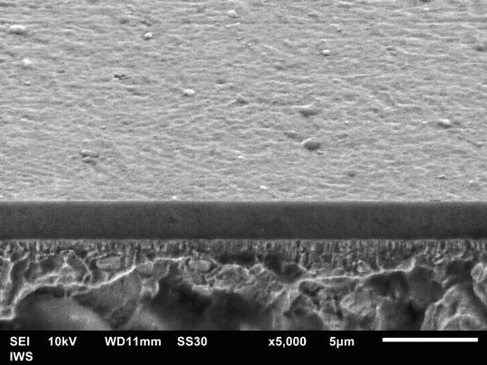 Mittels 90-Grad-Plasmafilterung hergestellte, etwa 2,5 µm dicke ta-C-Schicht. Schrägansicht auf die Bruchfläche im Rasterelektronenmikroskop. Die Partikelabtrennung des Fraunhofer IWS führt zu einer glatten, defektarmen Oberfläche und steigert die Lebensdauer belasteter Komponenten.(Bild:  Fraunhofer IWS)