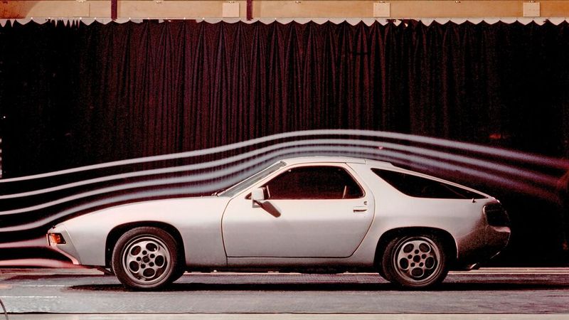 Ein 928 Prototyp im Windkanal, ca. 1977. Sein Transaxle-Prinzip unterscheidet sich etwas von dem des 924. Zwar verfügen beide über eine Kupplung am Motor, die die Kraft über eine gelenklose, mit Motordrehzahl rotierende Welle zum hinten eingebauten Getriebe überträgt und beim dem Motor und Getrieb mit einem starren Hüllrohr verbunden sind, in dem die Welle lief, doch während beim 924 das Getriebe hinter der Hinterachse sitzt, ist es beim großen Bruder vor dieser platziert. (Bild: Porsche AG)