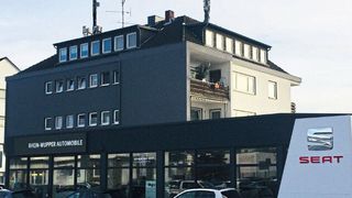 Das Seat-Autohaus an der Lützenkirchener Straße in Leverkusen liegt im Erdgeschoss eines Mehrfamilienhauses. Auffällig ist der „Corner Wall“, ein abgeschrägtes Eckelement mit silbernem Seat-Logo und rotem Schriftzug.  (Bild: Schormann)