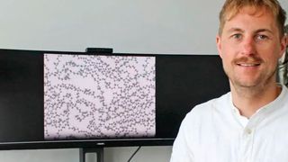 Prof. Dr. Christopher Kuenneth von der Universität Bayreuth vor dem neuentwickeltem digitalen System „polyBERT“. Der Bildschirm zeigt die atomistische Struktur eines Polymers mit Kohlenstoff-Atomen (graue Kugeln) und Wasserstoff-Atomen (weiße Kugeln). (Bild: UBT / Chr. Wißler)