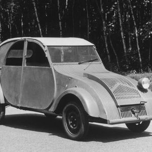 Citroën-Direktor Pierre-Jules Boulanger erteilte 1934 den Auftrag, einen minimalistischen Kleinwagen zu entwickeln. Die Anforderungen lauteten angeblich: „Entwerfen Sie ein Auto, das Platz für zwei Bauern in Stiefeln und einen Zentner Kartoffeln oder ein Fässchen Wein bietet, mindestens 60 km/h schnell ist und dabei nur drei Liter Benzin auf 100 Kilometer verbraucht. Außerdem soll es selbst schlechteste Wegstrecken bewältigen können und so einfach zu bedienen sein, dass selbst eine ungeübte Fahrerin problemlos mit ihm zurechtkommt. Es muss ausgesprochen gut gefedert sein, sodass ein Korb voll mit Eiern eine Fahrt über holprige Feldwege unbeschadet übersteht. Und schließlich muss das neue Auto wesentlich billiger sein als unser ,Traction Avant‘. Auf das Aussehen des Wagens kommt es dabei überhaupt nicht an.“(Bild:  PSA)
