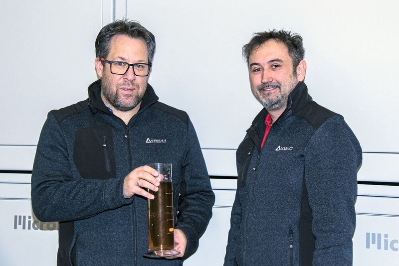 Tobias Raggl (links) und Anton Pfanner betrachten die gereinigte wässrige Lösung, die glasklar aus dem Filter kommt. Es sind weder Partikel über 3 µm noch Luftbläschen  enthalten. (Bild: Ceratizit)