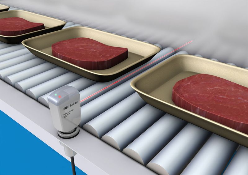 Eine SmartReflect-Lichtschranke im Hygiene-Design detektiert die Anwesenheit von Trays in der Fleischverpackung. (Bild: Baumer)