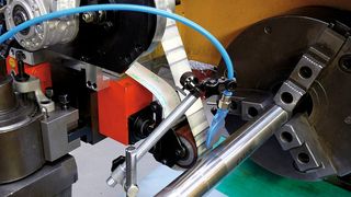 Der Versuchsaufbau an einem MAG-Boehringer-Drehautomaten besteht aus einem Mikro­finishing-Aufsatz mit Schleifband aus Aluminiumoxid, das mittels Druckluft und Gummi-Andrück­rolle im Eingriff gehalten wird. (Bild: Joliet)