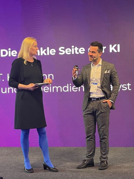 „Make it about people, make it entertaining.“ Profiler Mark T. Hofmann zeigte, wie die „dunkle Seite der KI“ so tickt und wie man ihr beikommt. Links: Moderatiorin Carmen Hentschel. (Bild: Vogel IT-Medien)