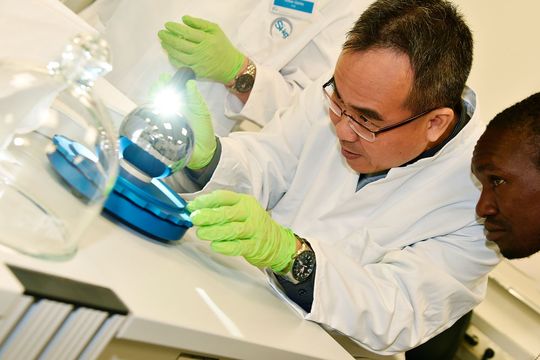 Shih Mean Lee (NMC, Singapur) und Wilson Ombati (KEBS, Kenia) überprüfen, ob sich Staubpartikel auf der Si-Kugel befinden. (Bild:  PTB)