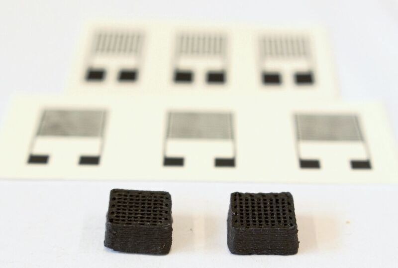 Neuartiger Werkstoff für gedruckte Schaltungen: Zwei Testquader von einem Zentimeter Breite aus dem 3D-Drucker. Im Hintergrund sieht man die gedruckten elektronischen Sensoren. (Empa)