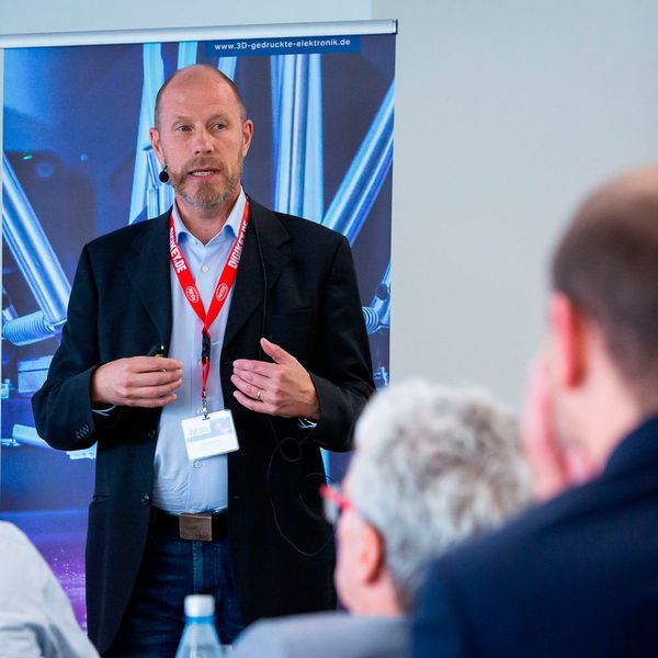 Pasi Pukkoo, VTT Finnland, präsentiert einen hybriden Ansatz: in ein additiv gefertigtes Bauteil hat er einen Sensor zur Zustandsüberwachung integriert.  (Bild: Stefan Bausewein)