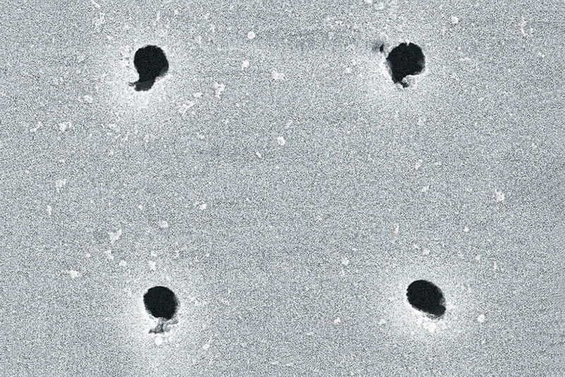 Elektronenmikroskopische Aufnahme von vier Bohrungen mit einem Austrittsdurchmesser von 1 µm mit 10 µm Abstand zueinander, eingearbeitet in eine 10 µm dicken Edelstahlfolie. (ILT)