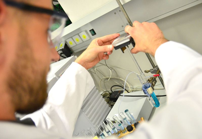 Davide Viscarelli installiert den Lichtleiter im Versuchsaufbau. Wie gleichmäßig er leitet, testet er mit einer Probe aus Wasser und dem abzubauenden Testfarbstoff Methylenblau. (FH Münster/Pressestelle)