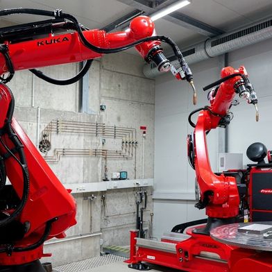 Für die BTU Cottbus‑Senftenberg hat ALOtec eine stationäre WAAM‑Anlage aufgebaut: zwei Kuka-Roboter KR120 R3100 im Master‑Slave‑Betrieb mit insgesamt 16 synchronisierten Achsen sowie Fronius iWave/TPS‑Technik ermöglichen den schnellen, schichtweisen Aufbau großer Metallbauteile.

 (Bild: ALOtec Dresden GmbH)