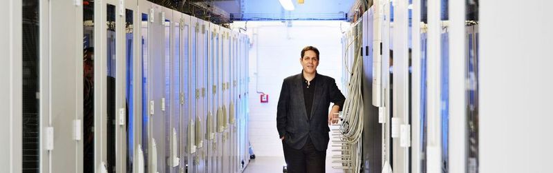 Idee in der Kantine: Bruce Allen, Direktor am Max-Planck-Institut für Gravitationsphysik in Hannover, diskutierte im Jahr 1999 beim Essen mit einem Kollegen über die Möglichkeit, Daten von Gravitationswellendetektoren durforsten zu lassen. Daraus entstand schließlich Einstein@Home, an dem bisher mehrere Hunderttausend Menschen weltweit teilgenommen haben. Der Atlas-Cluster, neben dem Allen hier steht, spielt in dem Netzwerk eine zentrale Rolle. (Bild: Frank Vinken)