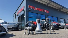Kollaboratives Trio vor der Autowelt Prusseit in Horb am Neckar: Der rollende Orionstar-Roboter (Mitte) bildet das zentrale Nervensystem, der Quadruped von Neura Robotics (l.) kartografiert das Gelände, der Unitree-Humanoide übernimmt Botengänge wie das Holen von Fahrzeugschlüsseln. (Bild: Achter – VCG)