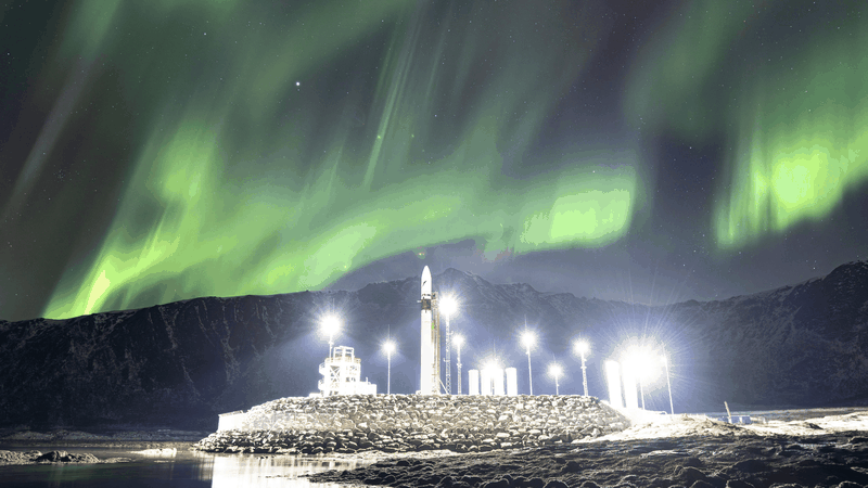 A Spectrum vehicle on its illuminated launch pad at Andøya Spaceport beneath sweeping curtains of northern lights.(Source:  Isar Aerospace/ESA Standard Licence)